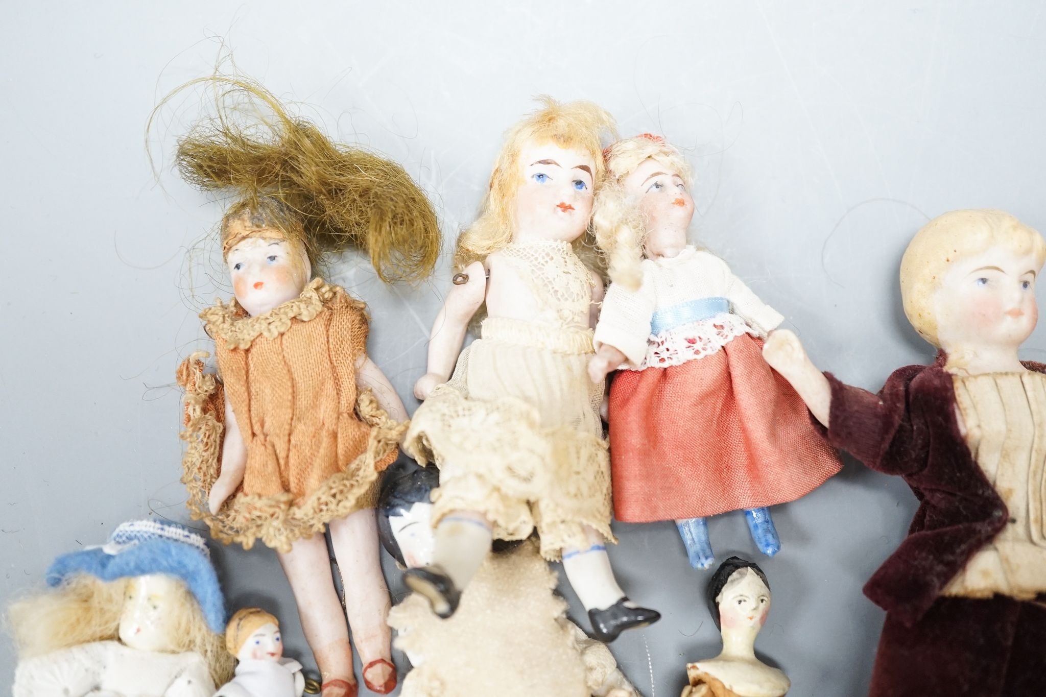 A collection of miniature bisque dolls and another larger doll in a wooden cradle, 11 dolls in total., Cradle 23.5 cms long.